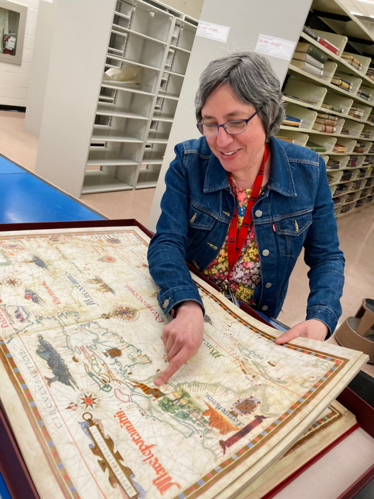 A librarian is pointing at a spot on a large map.